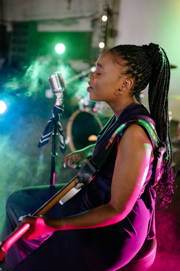 A female musician passionately singing and playing guitar under colorful stage lights.