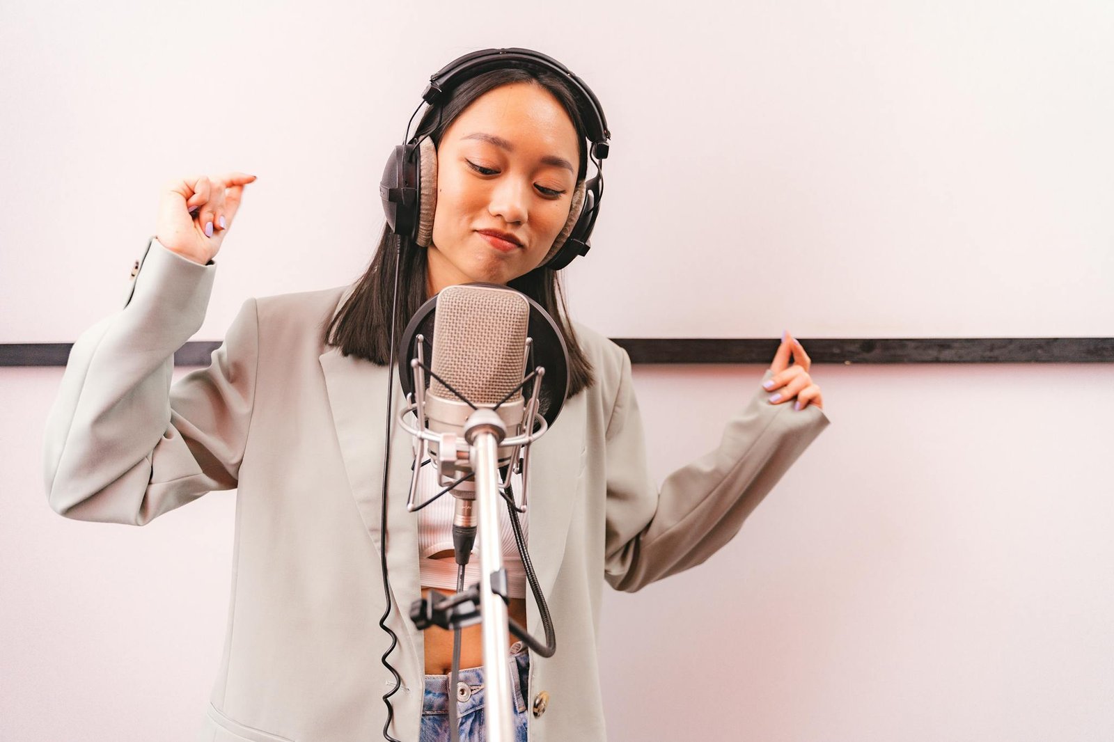 Asian woman singing in recording studio with microphone and headphones, expressing creativity.